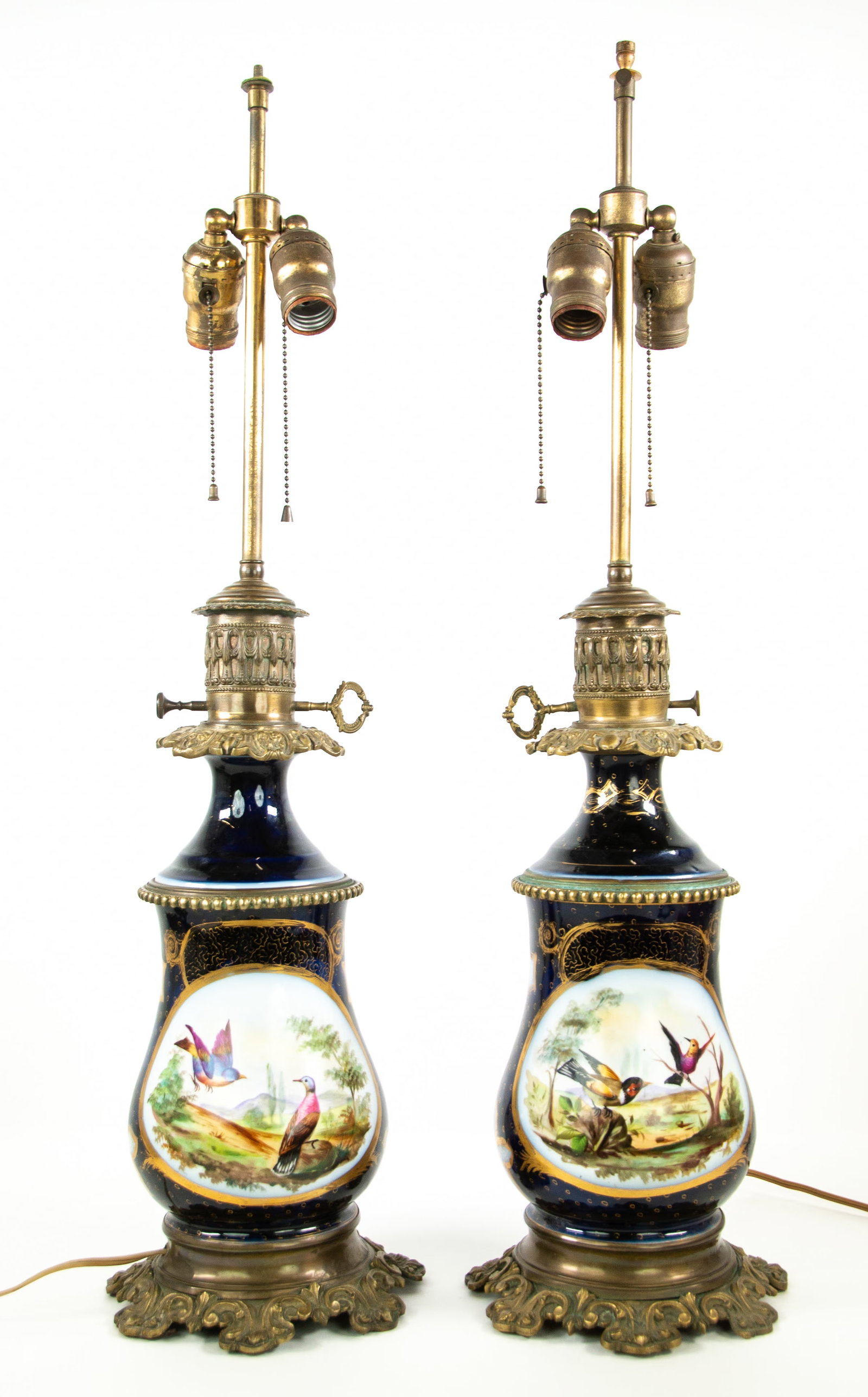 Pair of Old Paris Style Porcelain Lamps: Qualifies for in-house shipping---Each having a cobalt blue ground with gilt accents, one side having a center cartouche with hand painted landscape and birds, other side having a center cartouche wit