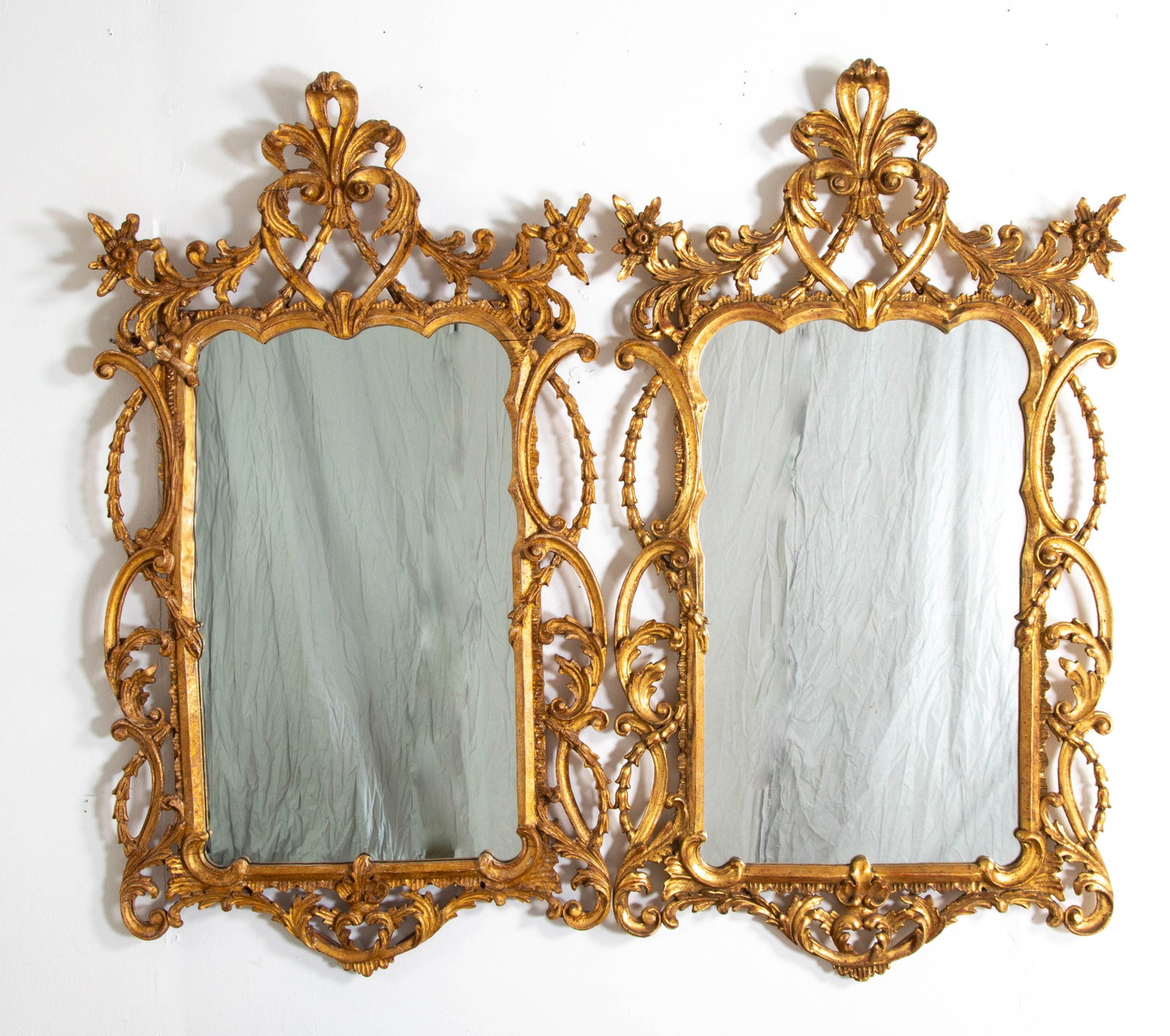 Pair of La Barge Italian Carved Giltwood Mirrors: Each having a pierced crest with fleur-de-lis at center flanked by scrolling leafy flower stems, above a shaped rectangular mirror surrounded by bellflower ropes and serpentine scrolls, bottom edge wi