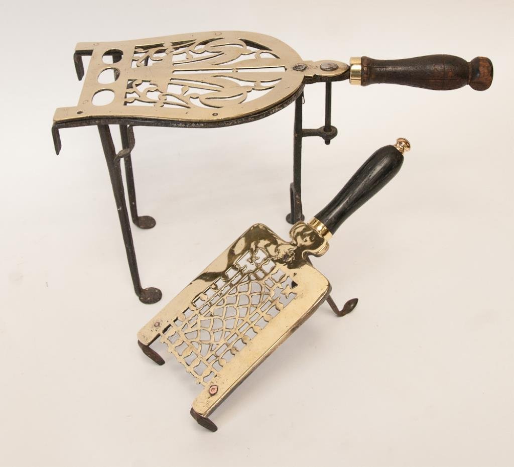 2 Hand-Wrought Iron & Brass Trivets: English, early 19th century: 1. Pierced brass horseshoe shaped plate, set on an iron tripod frame with penny feet, wood handle, 9 1/2"H, 7 1/2"D, 17"L; 2. Fender trivet with pierced brass plate set on