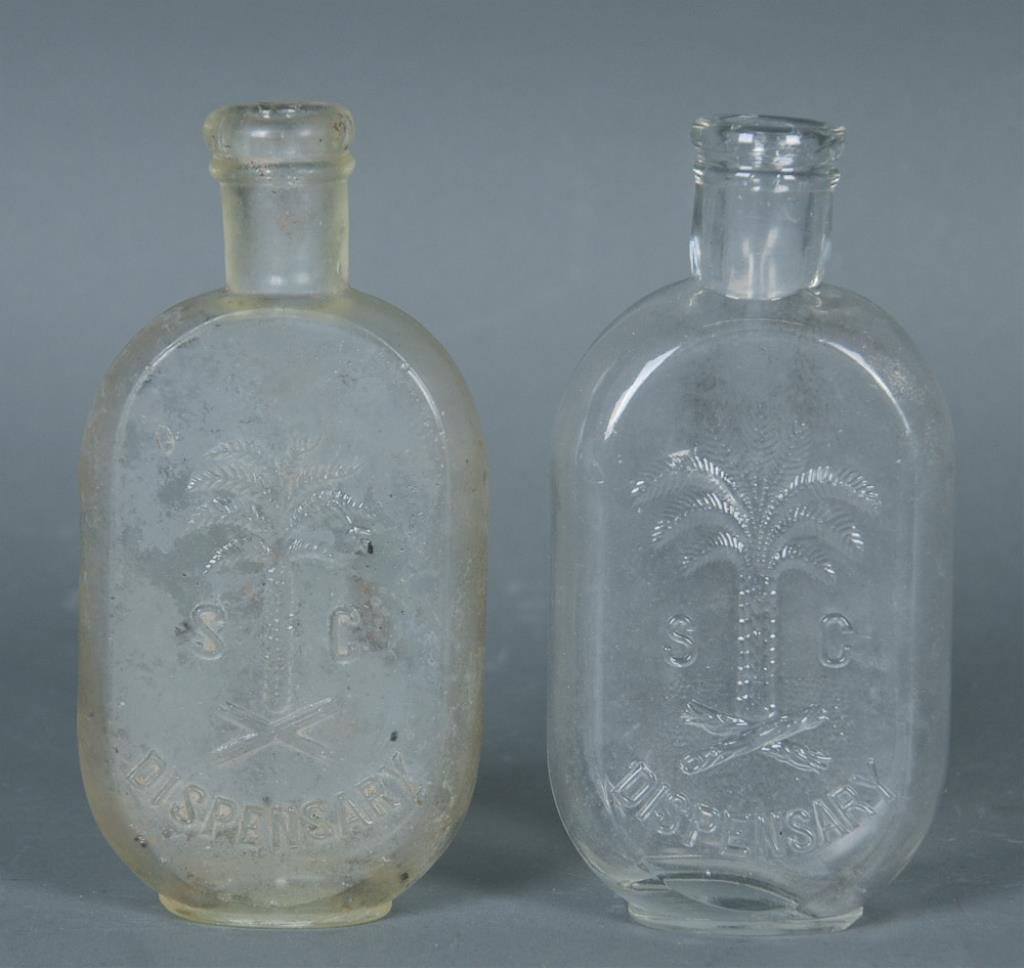 2 South Carolina Dispensary JoJo Flasks: Two clear half pint flasks with Palmetto tree, one similar to No. 140 with the exception being the posterior log is made up of wavy lines and both ends are broken, no maker's mark; other No. 127, E.P.