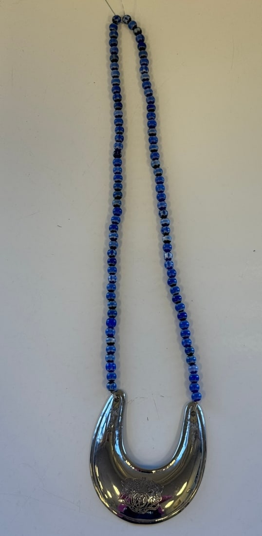 U-SHAPED/CRESENT "HORSE BRASS" NECKLACE: U-SHAPED/CRESENT NECKLACE SUSPENDED ON BLUE GLASS BEAD STRAND."HORSE BRASS' FORM WITH APPLIED HERALDIC CREST.3.5"W X 4" L NECKLACE IS 13" LONGPROVENANCE: ESTATE OF DOUG DIVISH NORTH EAST OHIO