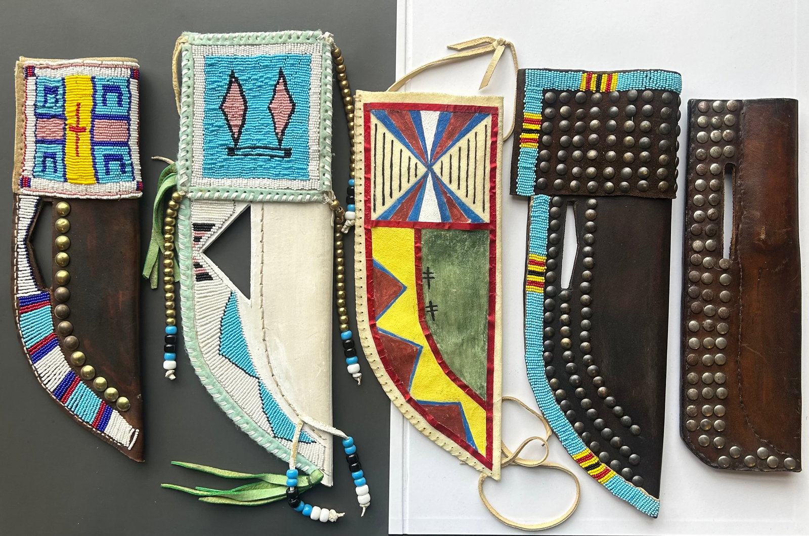 FRONTIER-STYLE & PLAINS INSPIRED KNIFE SHEATHS: EXCEPTIONAL COLLECTION OF 5 CUSTOM CRAFTED FRONTIER STYLE KNIFE SHEATHS. SHOWCASING A STRIKING VARIETY OF PLAINS INSPIRED BEADWORK, TRADITIONAL RAWHIDE PAINTING, AND CLASSIC WESTERN STUDDING. GREAT CO
