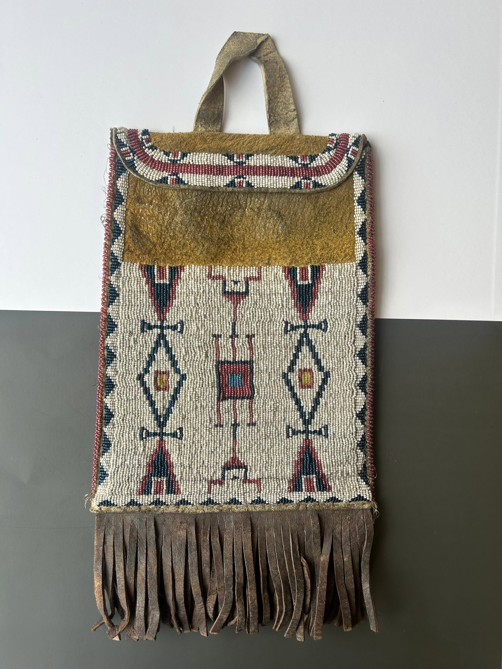 NATIVE AMERICAN PLAINS BEADED LEATHER POUCH: FINELY BEADED NATIVE AMERICAN LEATHER POUCH WITH LONG LEATHER FRINGE AND GEOMETRIC SEED BEAD DECORATIONS. POUCH MEASURES APPROX: 14" (INCLUDING FRINGE) X 8" . GOOD ANTIQUE CONDITION, LEATHER SHOWS EXP