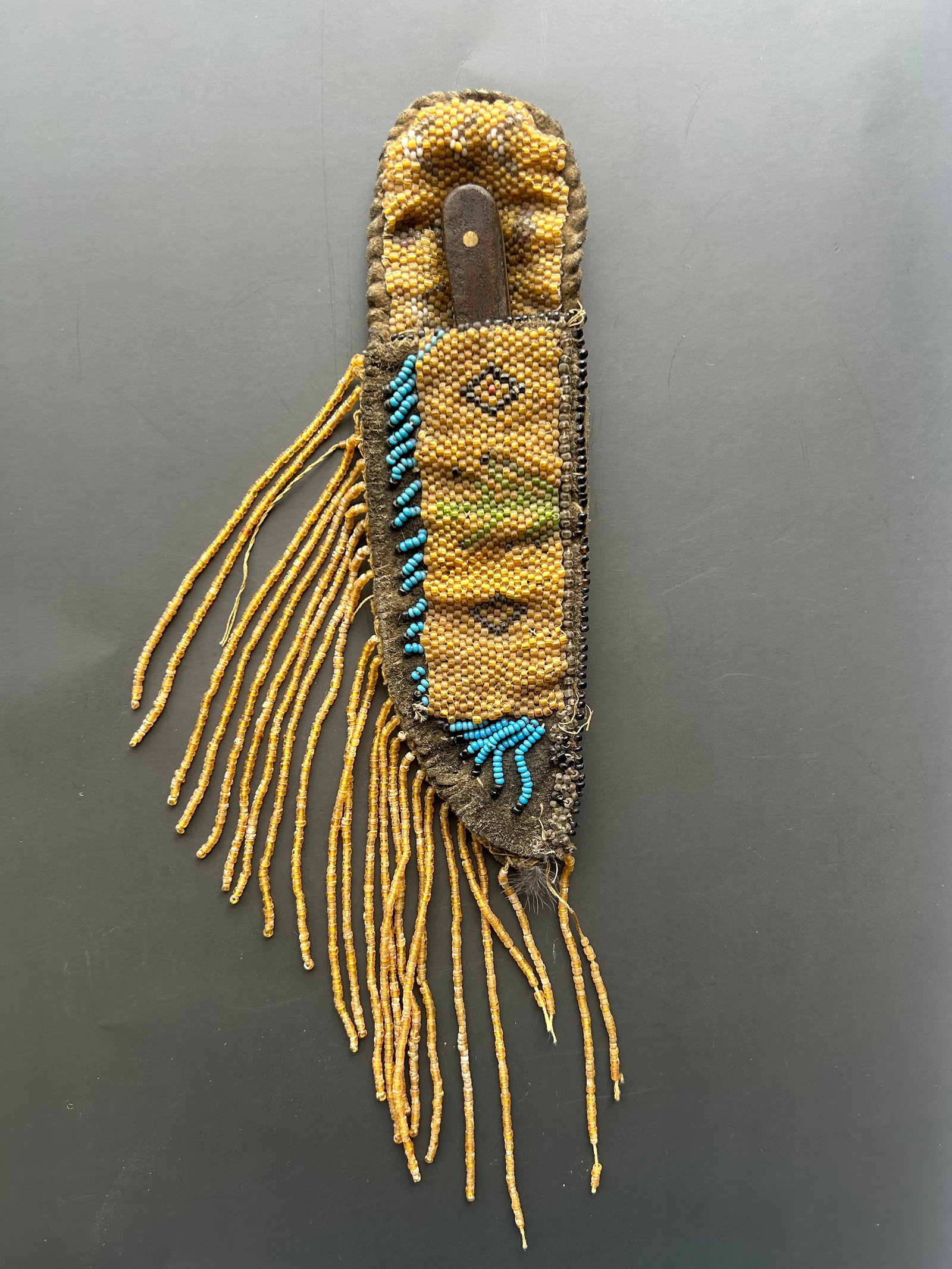 EARLY 20TH CENTURY NATIVE AMERICAN BEADED SHEATH: FINE HIDE SHEATH MEASURING APPROX. 7" IN LENGTH, DECORATED WITH GEOMETRIC SEED BEADWORK AND RETAINING EXTENSIVE GLASS TRADE BEAD FRINGE. ACCOMPANIED BY A KNIFE WITH A 3" BLADE, LIKELY LATER