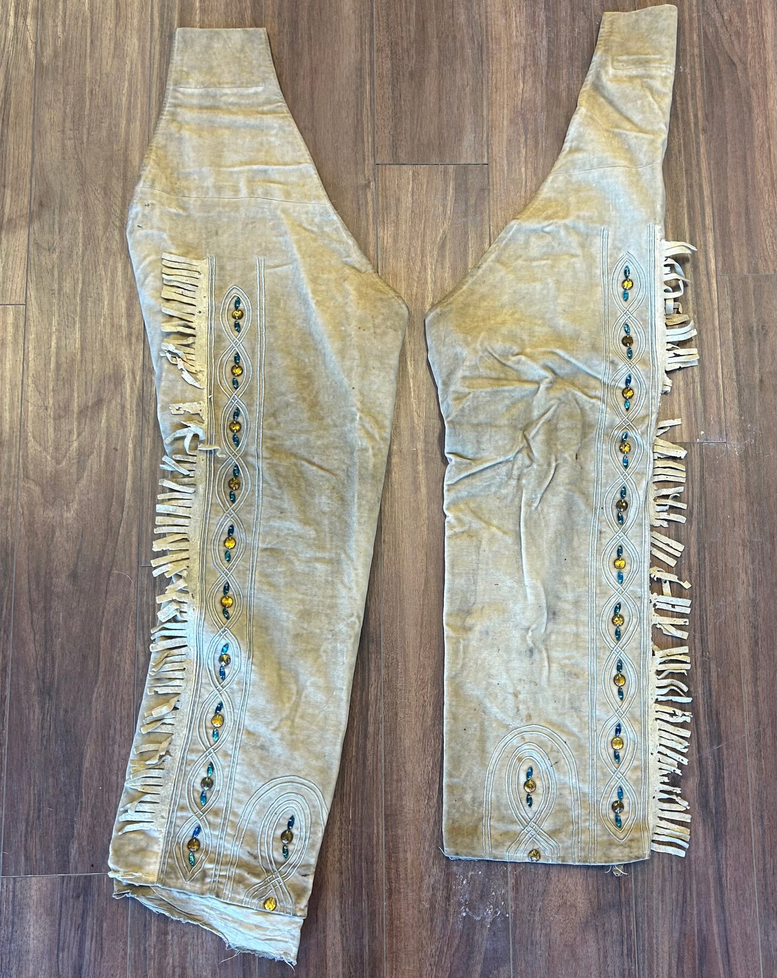 RARE PAWNEE BILL'S WILD WEST SHOW VELVET LEGGINGS: RARE PAIR OF PAWNEE BILL'S WILD WEST SHOW COSTUME CHAPS CONSTRUCTED OF TAN VELVET WITH COTTON LINING. DECORATED WITH APPLIED CORDWORK, FACETED AMBER AND BLUE GLASS JEWELS AND LONG FRINGE ALONG THE