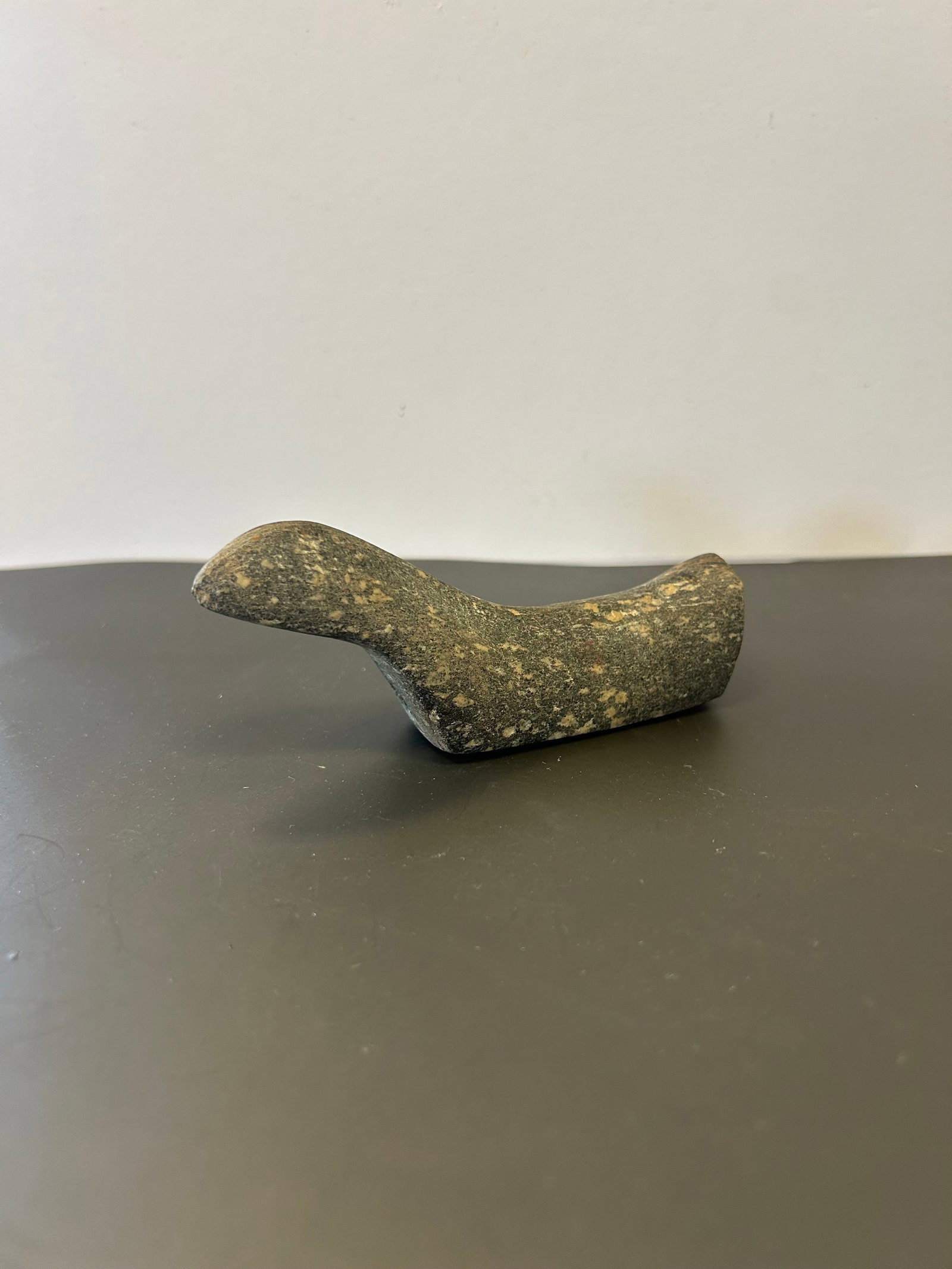PREHISTORIC GRANITE BIRDSTONE, PARKS COLLECTION: FINELY CARVED GRANITE BIRDSTONE FORM EFFIGY MEASURING APPROX. 4.5" IN LENGTH. FEATURES RAISED HEAD AND TAIL, SMOOTHED BODY, AND DUAL SUSPENSION PERFORATIONS THROUGH THE UNDERSIDE. RETAINS OLD