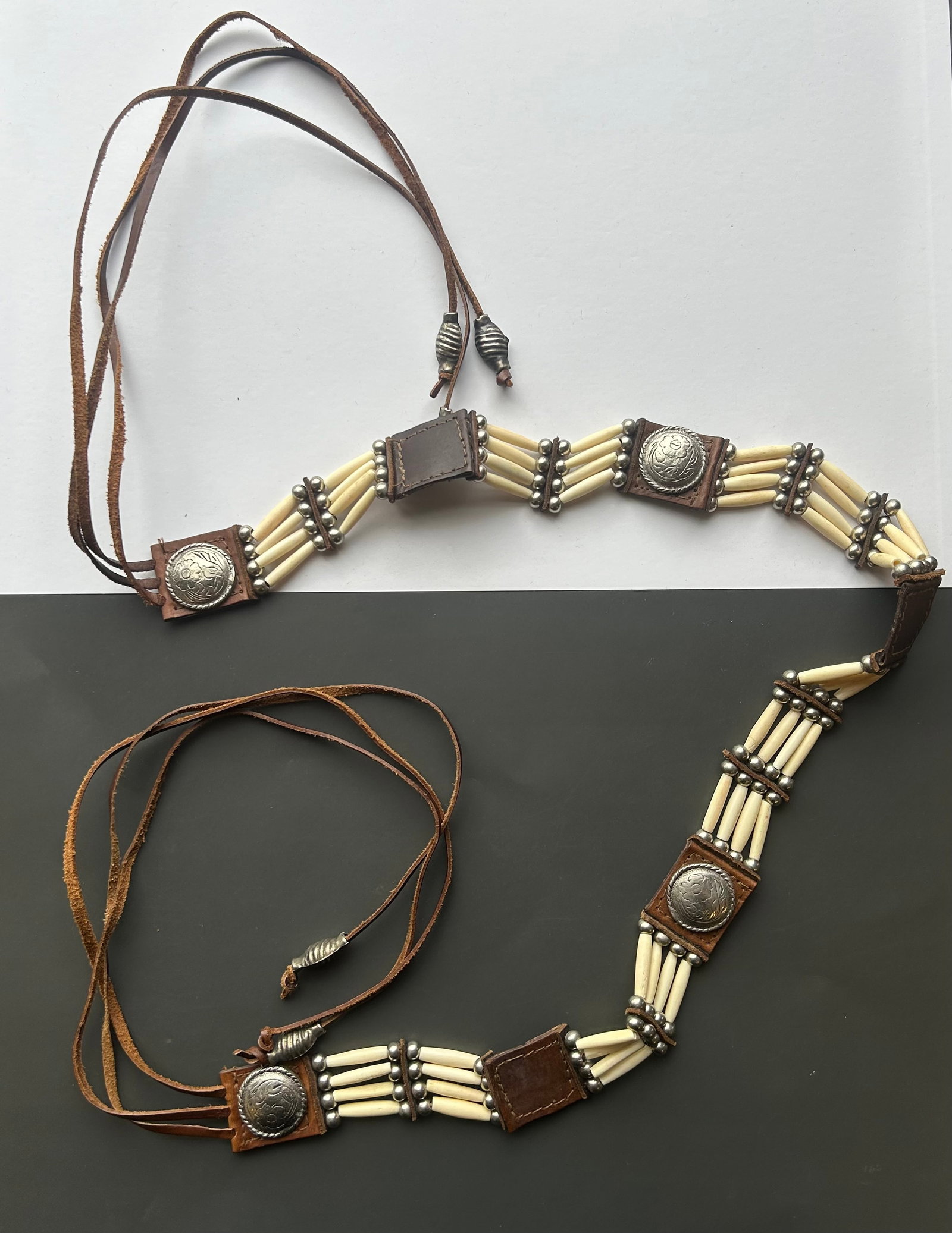 PLAINS STYLE BONE HAIRPIPE & CONCHO LEATHER BELT: LEATHER SASH OR BELT FEATURING MULTIPLE SECTIONS OF BONE HAIRPIPE BEADS SEPARATED BY METAL SPACER BEADS AND ACCENTED WITH FLORAL CONCHOS. LEATHER TIE CLOSURES WITH DECORATIVE METAL CONE TIPS. APPROX.