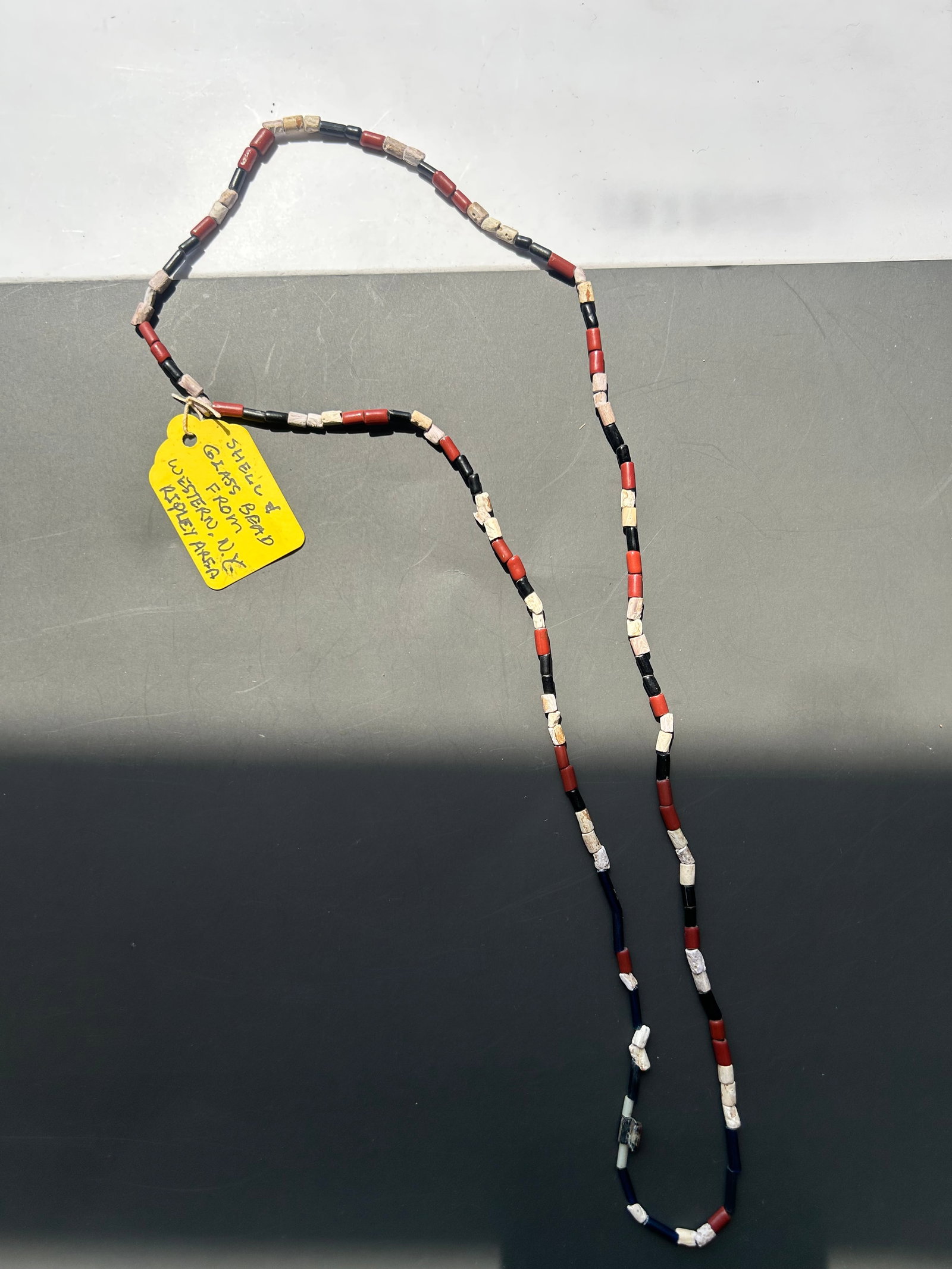 RARE WESTERN NEW YORK SHELL & GLASS TRADE BEADS: AN INTRIGUING STRAND OF ANTIQUE SHELL AND GLASS TRADE BEADS, RETAINING ITS ORIGINAL HANDWRITTEN IDENTIFICATION TAG READING: " SHELL & GLASS BEAD FROM WESTERN N.Y. RIPLEY AREA" BACK OF TAG HAS