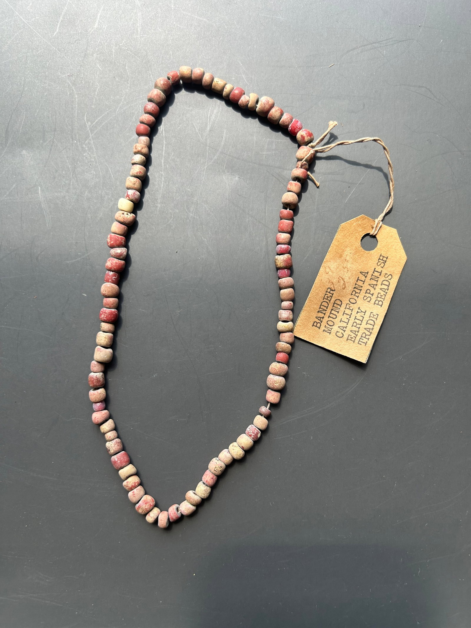 RARE CALIFORNIA MOUND TRADE BEAD STRAND: A REMARKABLE STRAND OF ANTIQUE TRADE BEADS PRESERVED WITH ITS ORIGINAL COLLECTOR TAG IDENTIFYING THE BEADS AS " BANDER MOUND, CALIFORNIA, EARLY SPANISH TRADE BEAD". THE STRAND CONSISTS OF NUMEROUS
