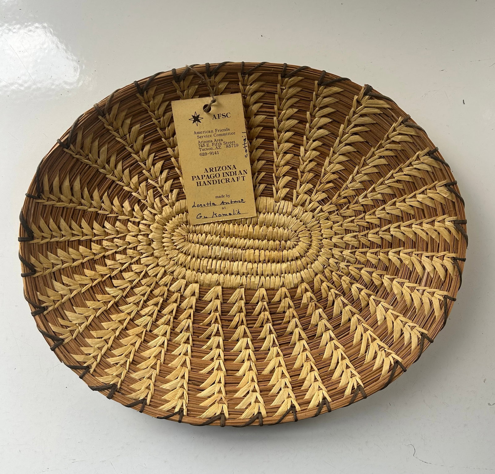 VINTAGE ARIZONA PAPAGO BASKET TRAY W/ ORIGINAL TAG: AUTHENTIC HANDWOVEN ARIZONA PAPAGO (TOHONO O'ODHAM) BASKET TRAY RETAINING ITS ORIGINAL AMERICAN FRIENDS SERVICE COMMITTEE HANDICRAFT TAG. THE TAG IDENTIFIES THE MAKER AND THIS STYLE WEAVE IS CALLED