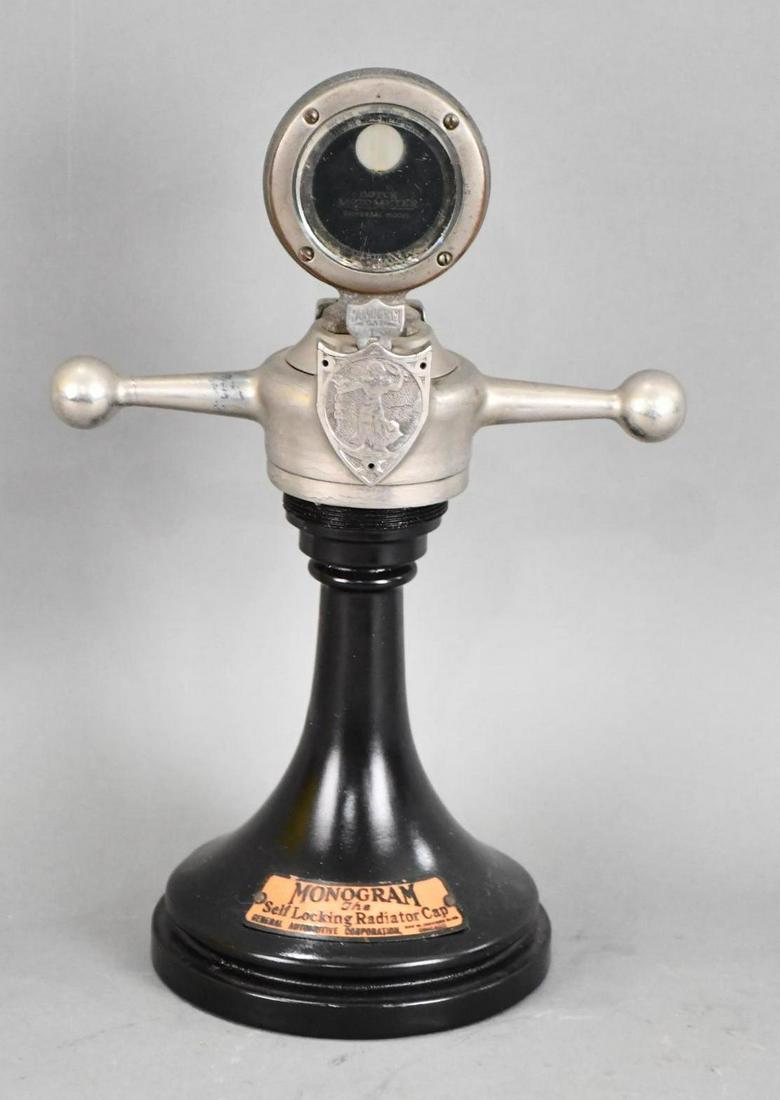 Monogram "The Self Locking Radiator Car" Counter-Top Display: rated 8.75, 13"T., the display has aluminum base has been repainted, tag has not, has a Boyce Moto Meter on top with a dog-bone.