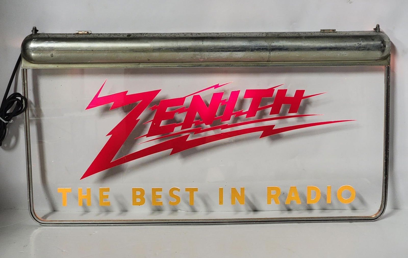 Zenith "The Best in Radio" Lighted Hanging Glass Sign: rated 9, 17'x30", the lighted glass sign is in very good condition, metal light box at the top has light wear, lights nicely.