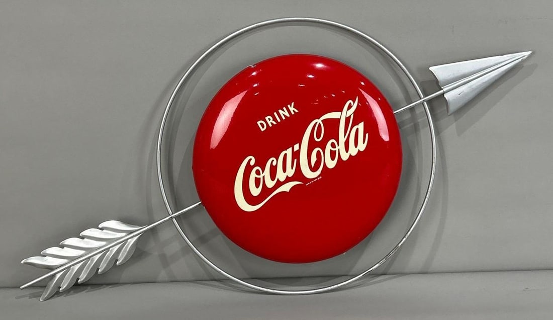 Drink Coca-Cola 12" Button Sign W/ Arrow Attachment: (Rated 9.0). 12" dia. This SST sign has excellent color and shine throughout. Sign shows light surface scratches in the field and on the outer edge. Sign has mounting brackets attached. Marked, "A-M S