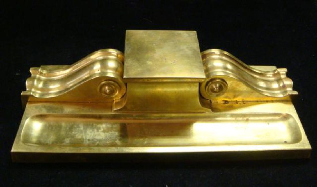 BRADLEY & HUBBARD Gilt Bronze Inkwell:: BRADLEY & HUBBARD Gilt Bronze Inkwell: Single Inkwell with Glass Liner Flanked by Scroll Sides. Pen Holder in Front. Cast Iron Base with Holes. 10 5/8" X 4 3/4", 2 3/8"T. (150-250)