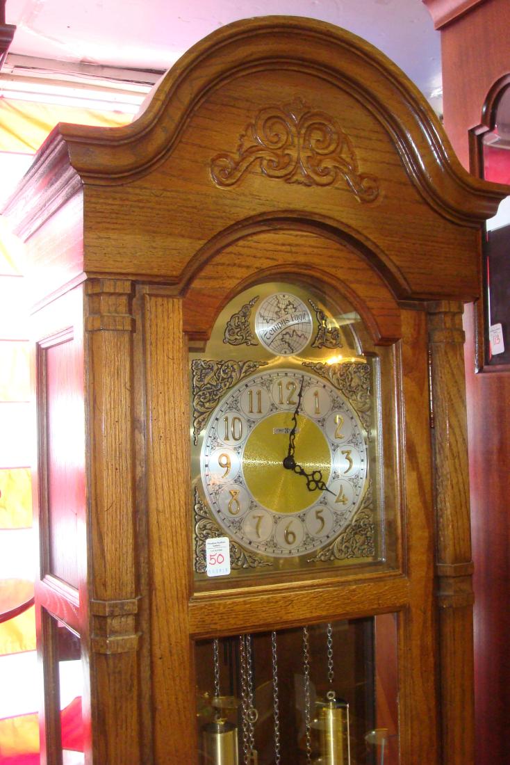 HOWARD MILLER Long Case Clock with Pendulum, Weights:: HOWARD MILLER Long Case Clock with Pendulum, Weights: CA 1978. Full Glass Lower Door Shows Three Brass Weights and Pendulum. Raised Arabic Numerals on Metal Face. Impressed Design on Arched Top. Seria