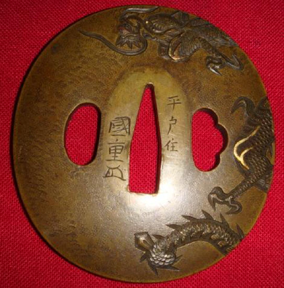 Signed Japanese SMTO KU TSUBA (Sword Guard) w/ Dragon:: Signed Japanese SMTO KU TSUBA (Sword Guard) w/ Dragon: Intaglio Dragon Swirls on Each Side of Signed Brass Tsuba. Oval 3" x 2 3/4". Very Fine Detail. SMTO KU is a Mixture of Gold and Brass. (300-500)