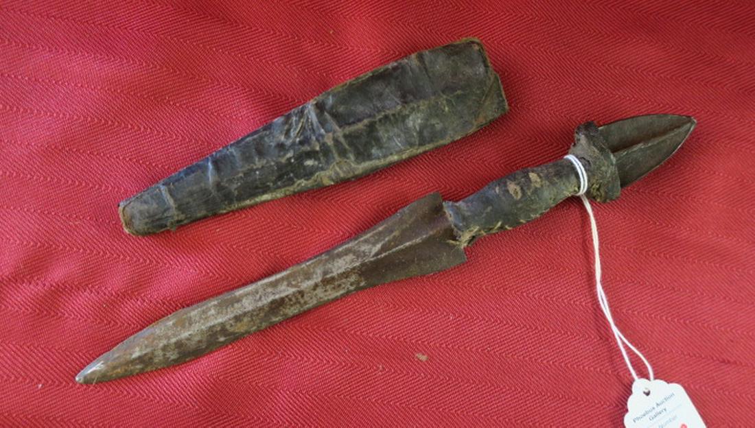 Antique Central African Dagger w/Skull Cracker Pommel:: Antique Central African Dagger w/Skull Cracker Pommel: Very Old Leather Covered Sheath and Cross Grips. Skull Cracker Pommel. 10" LOA, Double Sided 6" Blade with Minor Decoration. (300-600)