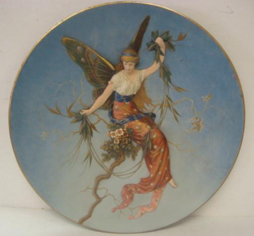 METTLACH Plaque with Relief Figure of Winged Woman: METTLACH Plaque with Relief Figure of Winged Woman: Form #1696, Ca 1887. Blue Ground with Castle Mark on Back. Artist G.F. Schultz. 16 1/4"D. (400-650)