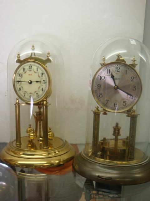 2 SCHATZ & KUNDO German Anniversary Clocks:: 2 SCHATZ & KUNDO German Anniversary Clocks: 10 1/2"T Schatz Clock with Silver and Gold Tone Metal Face. Pendulum Needs Reattaching. 11"T Kundo Clock Marked Made in Western Germany. Both with Glass Dom