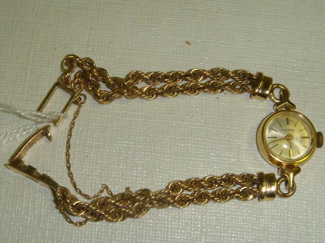 14KT Yellow Gold Ladies BUCHERER Wrist Watch: 14KT Yellow Gold Ladies BUCHERER Wrist Watch: Watch & Yellow Gold Double Rope Band are 14KT Gold. 1/2"D Round Face Having Gold Numeral Marks and Sapphire Crystal. 18.7 Grams 6"L with Safety Chain. Few