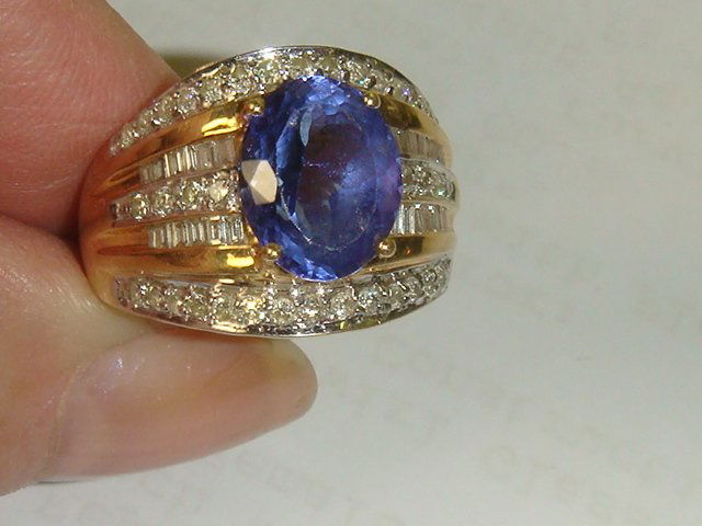 14KT Tanzanite and Diamond Ladies Dinner Ring: 14KT Tanzanite and Diamond Ladies Dinner Ring: Center 3 CT Oval Tanzanite Surrounded by 1 1/2 CT of Diamonds, 40 Small Round and 24 Baguettes. Set in Wide Yellow Gold Band, Size 7 1/2. 4.8 dwt with St