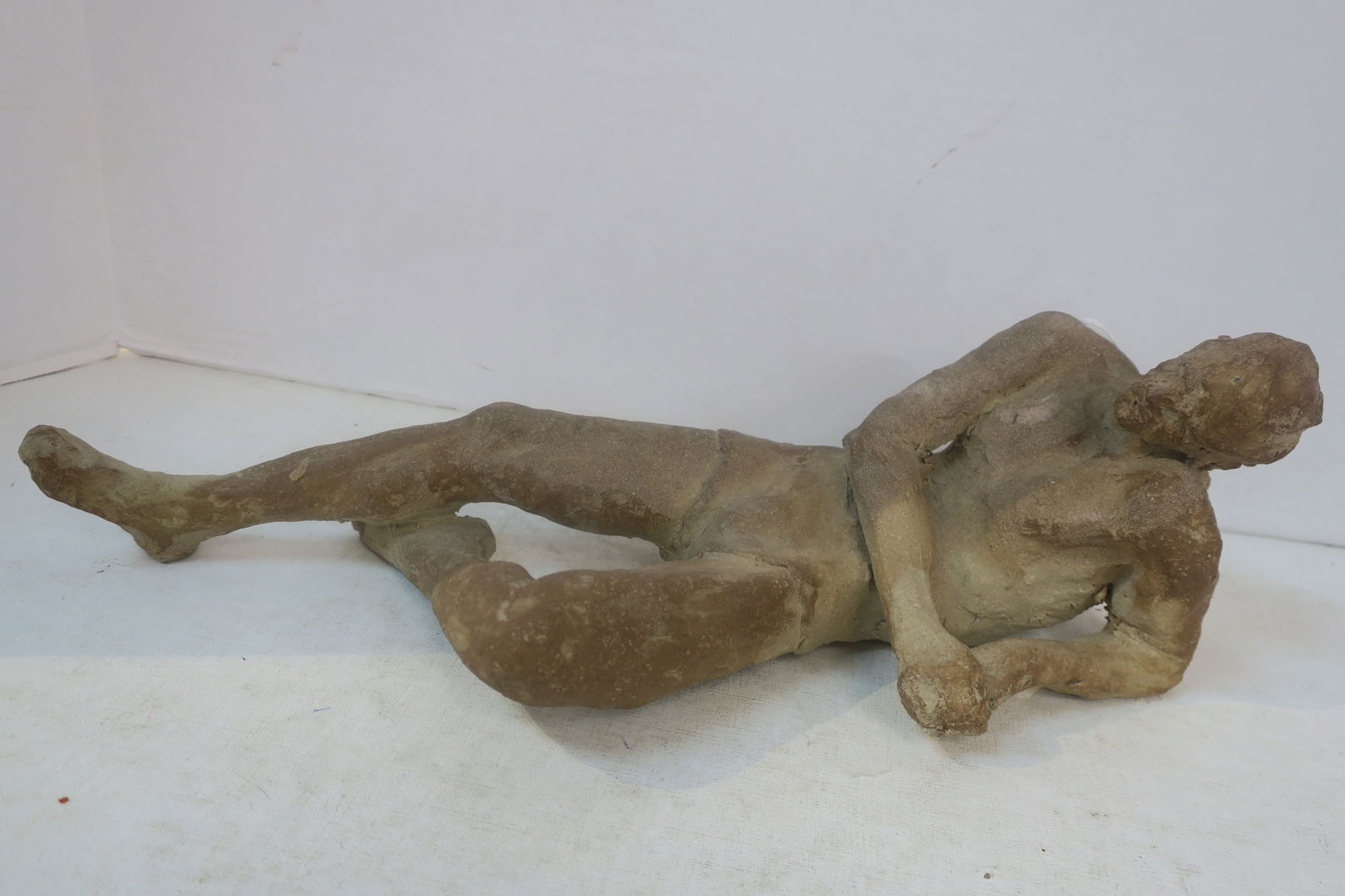 Reclining Nude Male Clay Figure:: Reclining Nude Male Clay Figure: Man in a Relaxed Prone Position Resting on His Forearm with Right Arm Crossing in Front of His Chest, Bent Left Leg Onder the Opposing Knee. Unsigned. 15"L. (100-200)