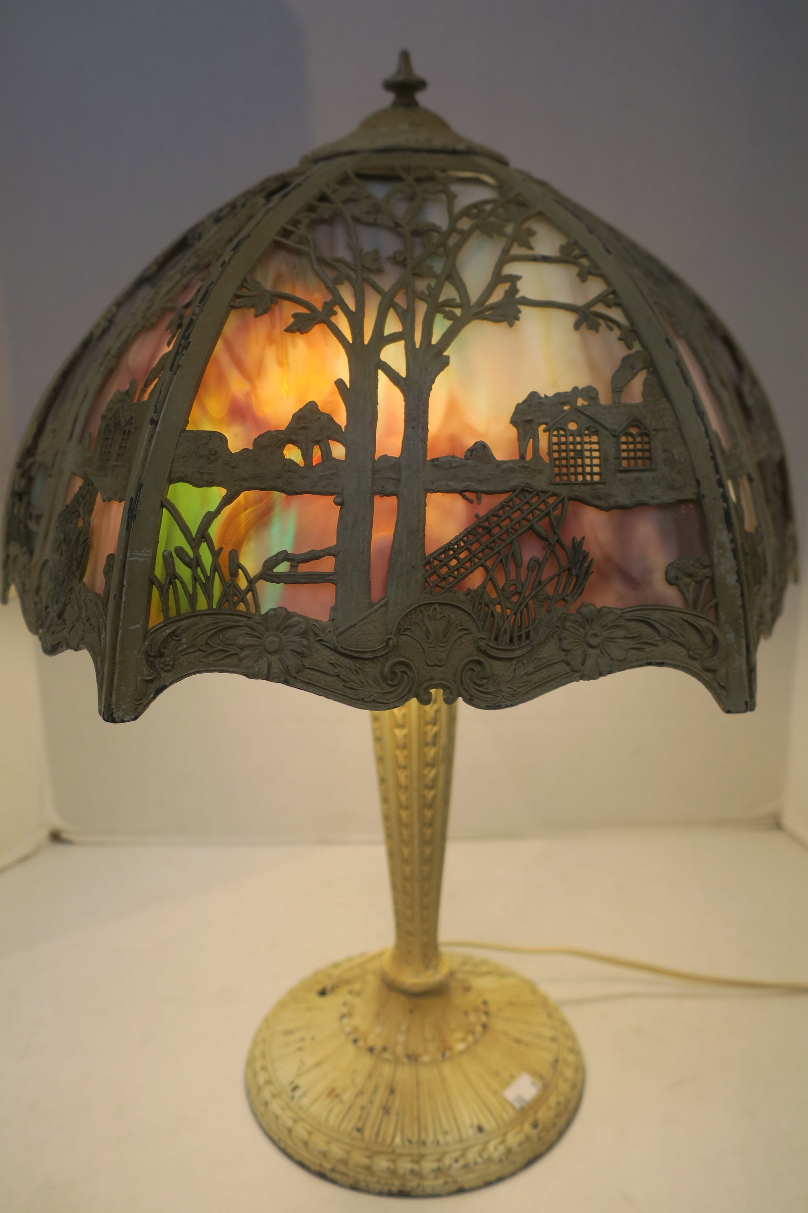 Vintage Pictorial Stained Glass Table Lamp:: Vintage Pictorial Stained Glass Table Lamp: Overlay Scene of Trees, House, Bridge of Cream Color Metal over Rainbow Stained Glass Panels. Hexagonal Domical Shade on Pedestal Lamp, Round Foot. 20"Tall,