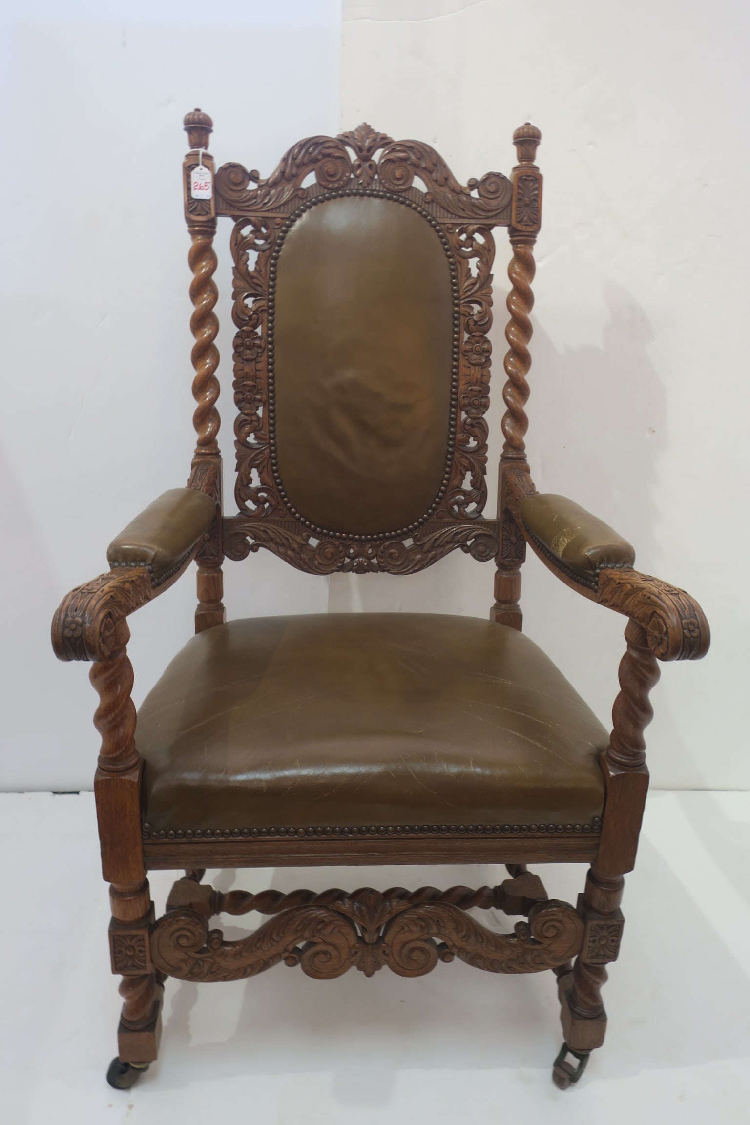 Heavily Carved Vintage Oak Throne Arm Chair:: Heavily Carved Vintage Oak Throne Arm Chair: Deeply Carved Foliate Arms, Back and Front Rail. Twist Arms and H Stretcher. Brown Lather Seat and Back insert. Minor Wear to Leather. Front Casters, Measu