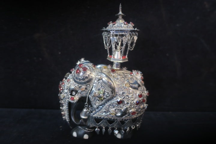 Srilankan Kandy Asian Elephant Figurine:: Carved Ebony Wood Body with Embossed Silver Overlay Parade Dress. The Ornate Handmade Figurine is Decorated with Gemstones-Garnet, Citrine, Peridot. He is in the Casket Bearer Holding the Tooth of Bud