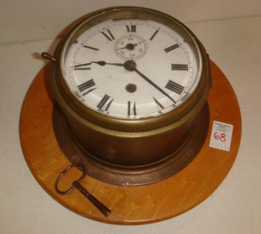 Ships Clock with Key on Wooden Base:: Ships Clock with Key on Wooden Base: 7" Diameter Clock with Key on Wooden Base Enameled Face and Brass, Works. Unmarked, Over Wound. 13" Round Wood Base. (300-500)