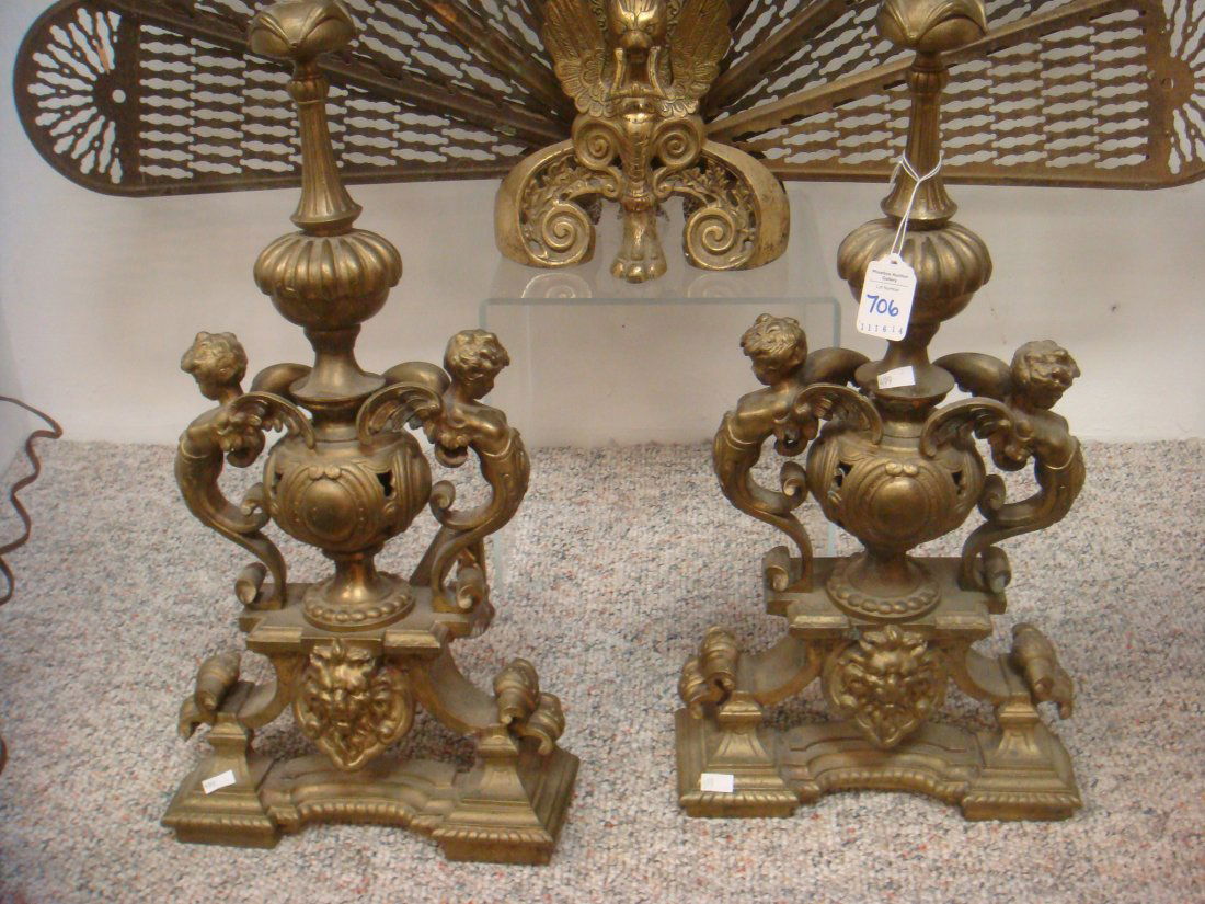 Pair of Winged Cherub Brass and Iron Chenets:: Pair of Winged Cherub Brass and Iron Chenets: Cherub Form Handles on Either Side of Pierced Urn Shape Over Lions Face. Rear 7" Log Support has Egg and Dart Design Along Top. Spire Shaped Finial with A