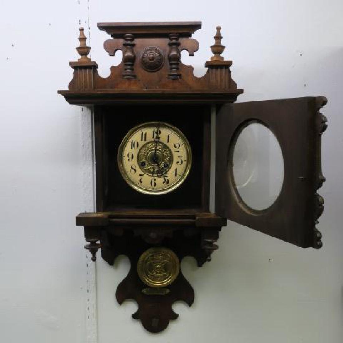 German Walnut Cased Wall Clock:: German Walnut Cased Wall Clock: Turned 1/2 Columns Flank Paper Face with Arabic Numerals. Floral Pressed Metal Center. Applied Leaves on Door. Key and Pendulum. 32"T, 16 1/4"W. (200-400)
