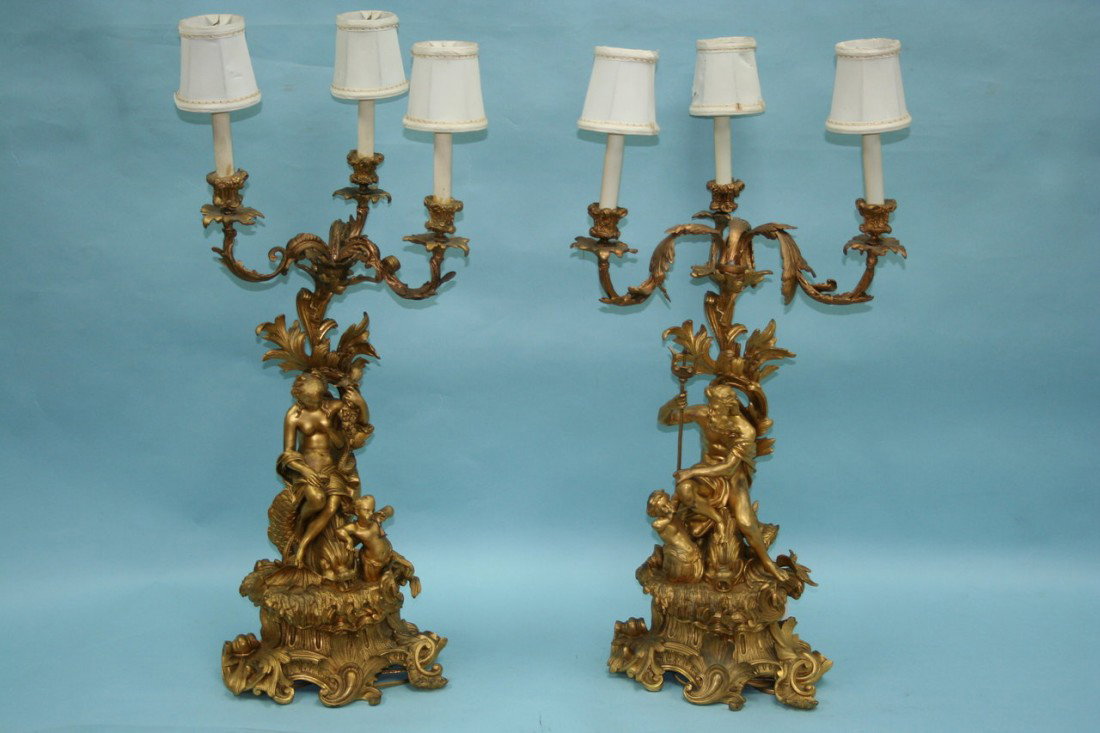 A pair of antique French gilt bronze candelabra. E: A pair of antique French gilt bronze candelabra. Each with elaborately cast scrolled base with mythological figures supporting three scollarmed lighting fixtures. Each 27" high.
