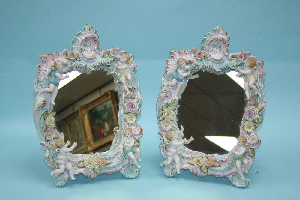 A pair of handpainted and gilt German Sitzend: A pair of handpainted and gilt German Sitzendorf porcelain table mirrors. Each of cartouche shape, decorated with four cherubs floating along a flower decorated frame. 17" high, 12" wide. Hallmarked.