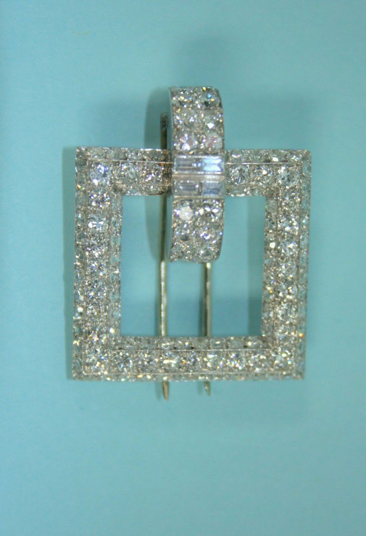 ART DECO _ An elegant platinum and diamond cl: ART DECO _ An elegant platinum and diamond clip brooch in form of a diamond set square buckle with a central ornament, mounted with a double row of good quality brilliant cut diamonds. Total diamond w