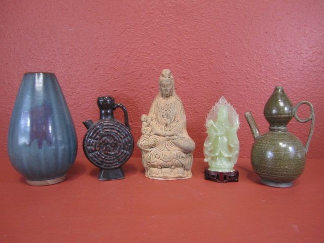 F29-2 LOT OF 5 CHINESE DECORATIVE ITEMS: Includes Chinese iron red & blue vase, jade Quan Yin on wood base, Celadon teapot, Quan Yin & Baby statue, and black & red teapot. Tallest item measures 10". Estimate $100 - $200
