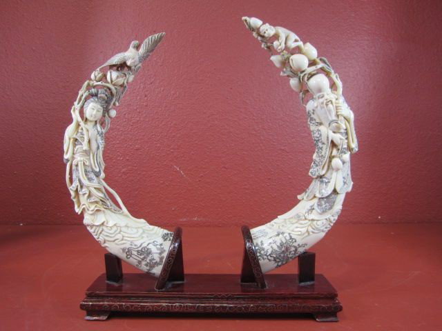 A11-2 PAIR OF CARVED IVORY TUSKS ON STAND: Signature illegible. Tusks measures 12 1/2" long overall on stand 13 3/4" tall x 14 1/2" wide. Estimate $3,000 - $3,500