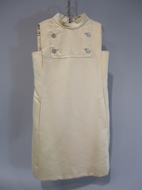 E14-1 VINTAGE 1960s COCKTAIL DRESS BY MALCOM STARR: Made for Elinor Simmons. Sleeveless champagne colored cocktail dress with mock t-neck and military style button front piece with crystal like inlay. Approximate size 8. Estimate $150 - $300 Starting B