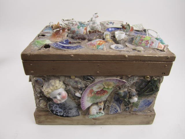 FOLK ART ANTIQUE KEEPSAKE CHEST: Large antique wooden chest with applies porcelain and pottery chards, cast iron toys,doll heads and part, and jewelry. Artist signed Thomas Studios Gerald T. Raney. Measures wide 19" tall 16" x deep 1