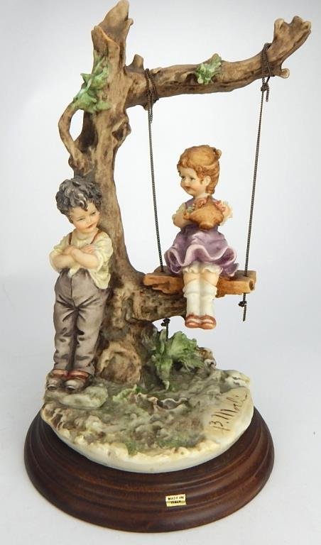 J65-92 CAPODIMONTE FIGURINE BY BRUNO MERLI: Boy leaning against tree flirting with girl in a swing. Makers mark and signature. Measures 11". Estimate $100 - $200 Starting Bid $20