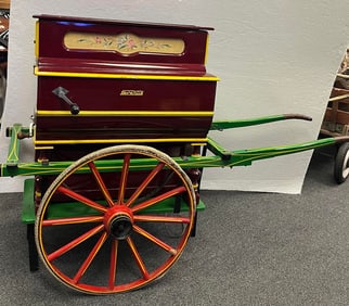 A vintage 'hurdy gurdy' music box on cart that can be hand cranked or used with electrical power.