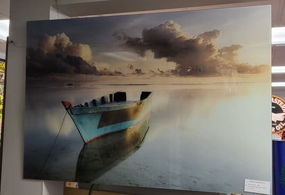 Photograph behind glass with hangers on the back of a Boat by the shore with Sky and Ocean