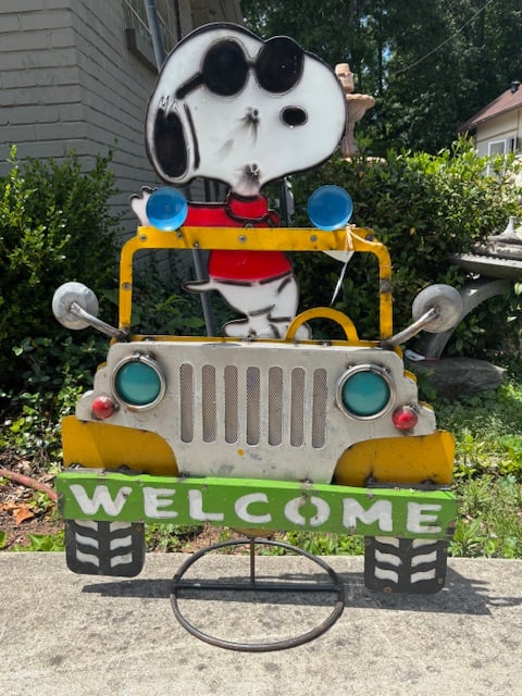 Vintage Snoopy in Yellow Jeep Metal “Welcome” Yard Art Sign /Peanuts: Painted Metal Yard Art of Snoopy wearing sunglasses driving a yellow jeep with “WELCOME” banner on the front bumper, freestanding. (37"H x 26"W.