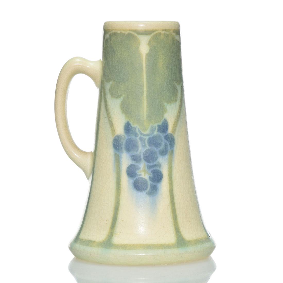 Rookwood Vellum tankard,Sax,grapes,1907, 1014 D, 7 1/4": Vellum glaze tankard with grapes decoration on either side, the work of Sara Sax in 1907. Marks include the Rookwood logo, date, shape 1014 D, an impressed V for Vellum, an incised V for Vellum glaze