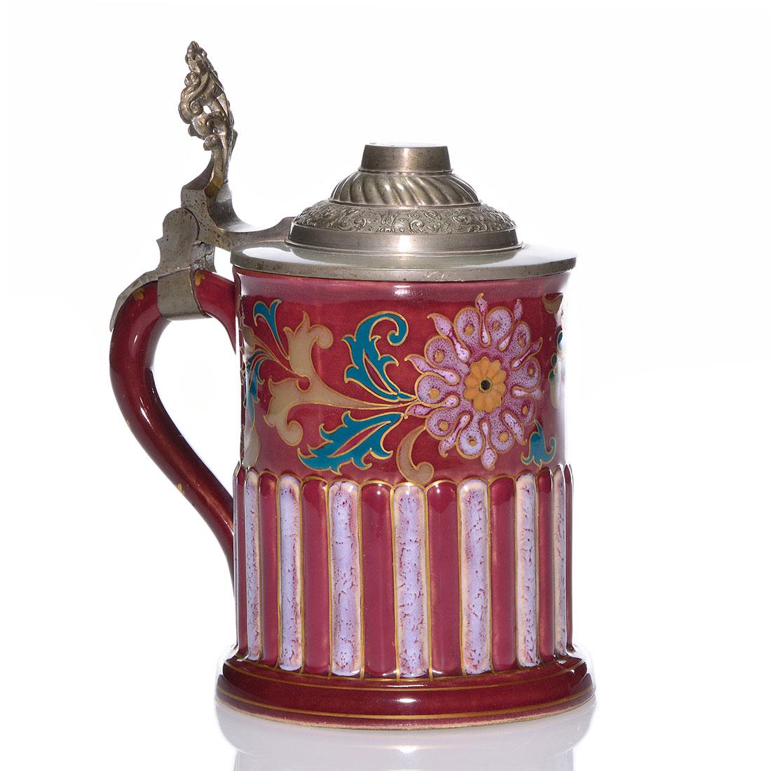 Zsolnay stein, floral, pewter cover, 6 3/4”, marks: Zsolnay Art Nouveau stein featuring exotic flowers and foliage in lilac and green highlighted by gold over a burgundy backdrop and encircled with a raised fence motif in two colors. The tiered pewter