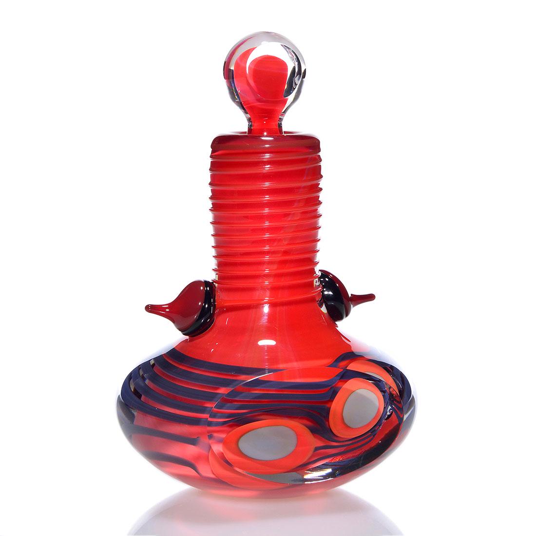 Robert Levin perfume & stopper, 6 1/2”, 1981, signed: Robert Levin perfume with stopper. Orange red overlaid with graphite gray ribbons and orange and gray buttons. A thick overlay of crystal has polished sides and applications of Hershey Kiss ornaments