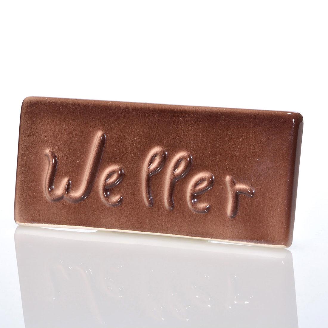 Weller dealer sign, 7 1/4” x 3 1/4”: Weller dealer sign covered in a brown high glaze. There is fine overall crazing and a small nick on the foot. Size is 3 1/4 inches high by 7 1/4 inches long.