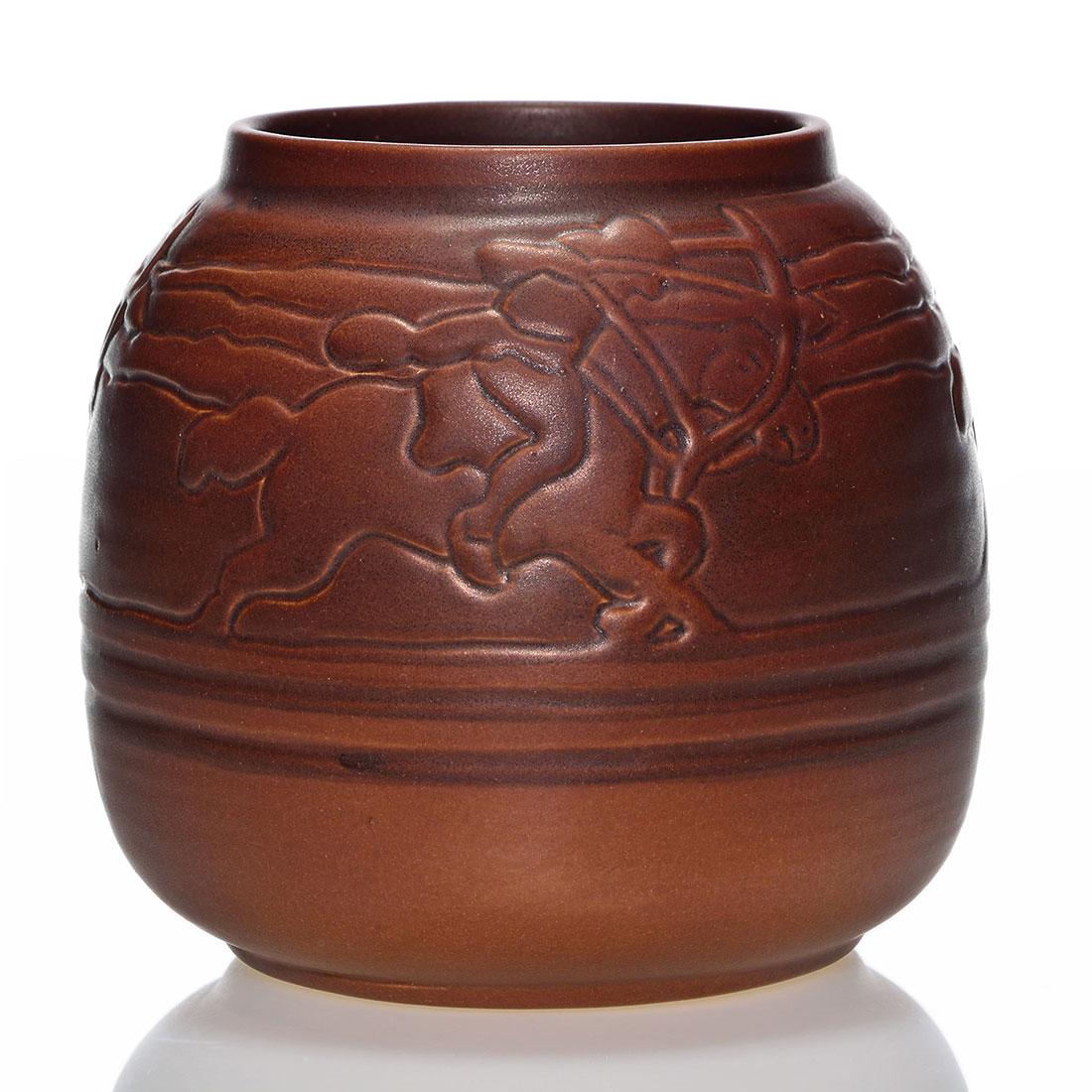 UND vase, Sioux on Horseback, Huckfield, 151, 5 3/8": UND vase decorated with a repeating pattern of Sioux on horseback with drawn bows, a Flora Cable Huckfield design, and covered with a brown mat glaze. Marked on the bottom with the blue UND logo and i