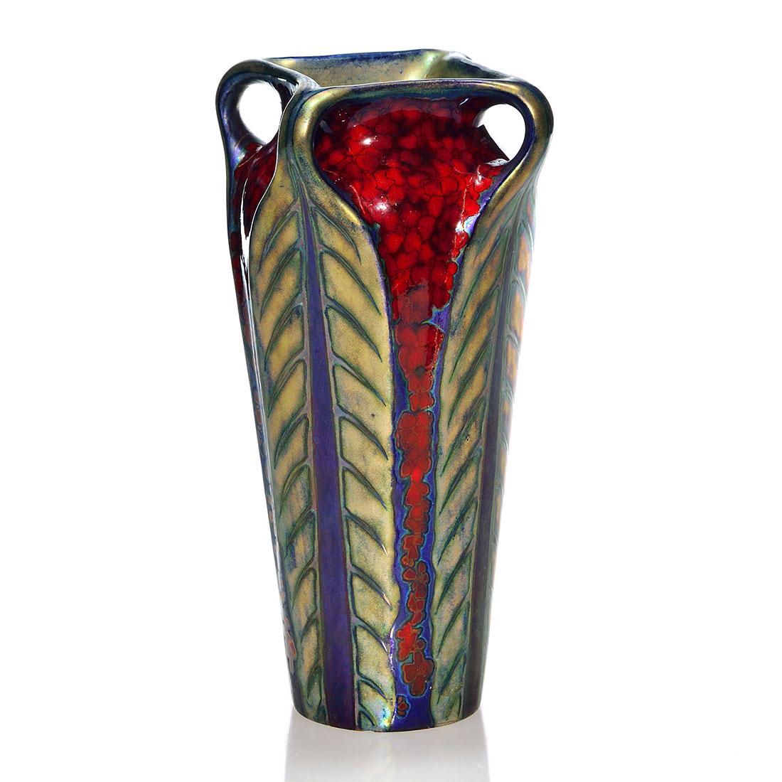 Zsolnay ruby Flambe lustre handled vase, 8 7/8”: Zsolnay ruby Flambe vase having four handles terminating into leaves covered by blue lustre and a coat of fired on gold, the under lying blue spreading to the edges for an appealing effect. Height 8 7