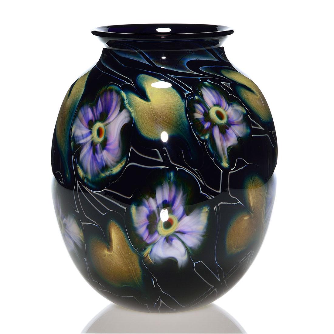 Charles Lotton Multi Flora vase, 10 3/4", black: Large Charles Lotton Multi Flora vase revealing black vines with ten purple white, ruby centered flower heads scattered among olive green foliage. The body is an opaque purple black color. Measures 10